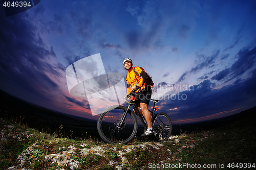 Image of cyclist standing with mountain bike on trail at sunset