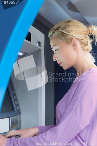 Image of Young lady withdrawing money at ATM machine entering her pin code.