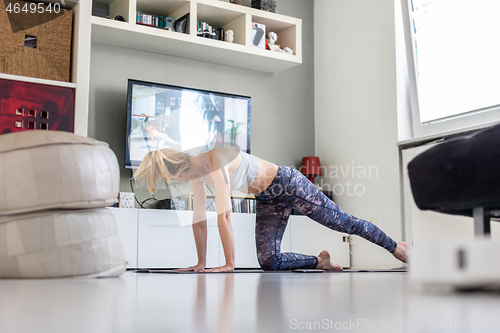 Image of Attractive sporty woman working out at home, doing pilates exercise in front of television in her living room. Social distancing. Stay healthy and stay at home during corona virus pandemic