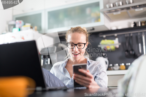 Image of Stay at home and social distancing. Woman in her casual home clothing working remotly from kitchen dining table. Video chatting using social media with friend, family, business clients or partners