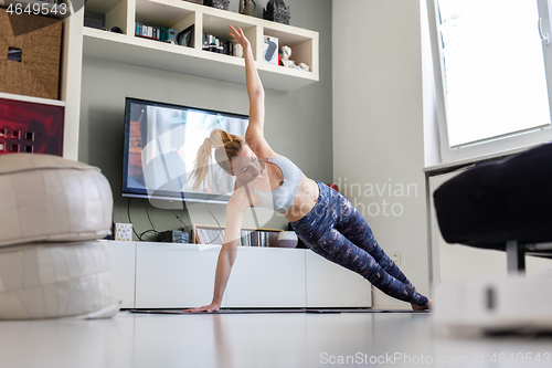 Image of Attractive sporty woman working out at home, doing pilates exercise in front of television in her living room. Social distancing. Stay healthy and stay at home during corona virus pandemic