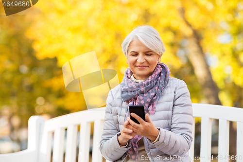 Image of happy senior woman with smartphone at autumn park