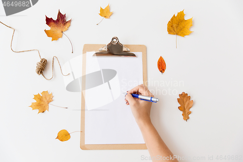 Image of hand writing on white paper on clipboard in autumn