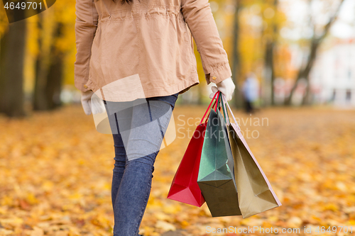 Image of woman with shopping bags walking along autumn park