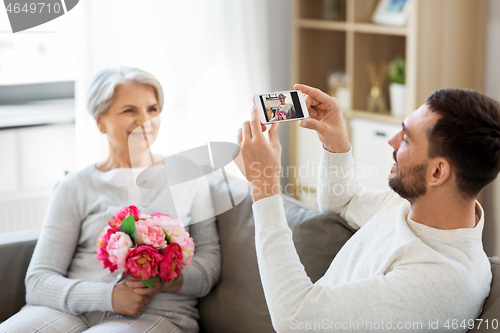 Image of adult son photographing senior mother at home