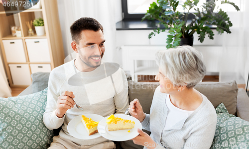Image of senior mother and adult son eating cake at home
