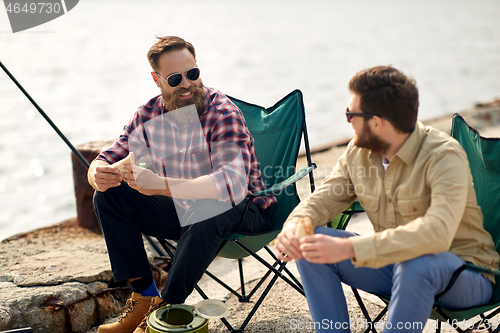 Image of happy friends fishing and eating sandwiches