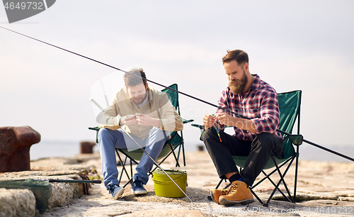 Image of friends adjusting fishing rods with bait on pier