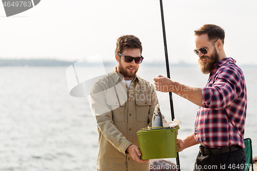 Image of male friends with fish and fishing rods on pier