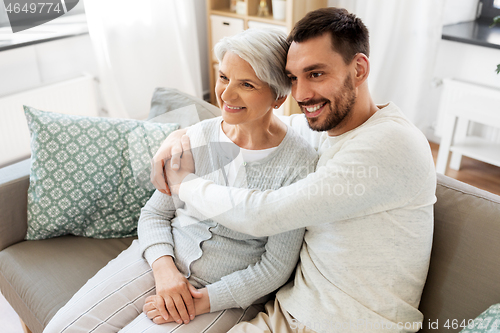 Image of senior mother with adult son hugging at home