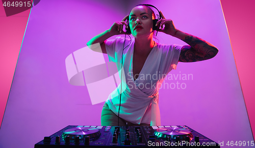 Image of Young caucasian female musician in headphones performing on purple background in neon light