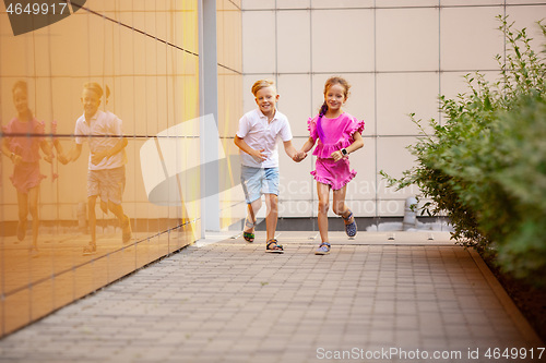 Image of Two smiling kids, boy and girl running together in town, city in summer day