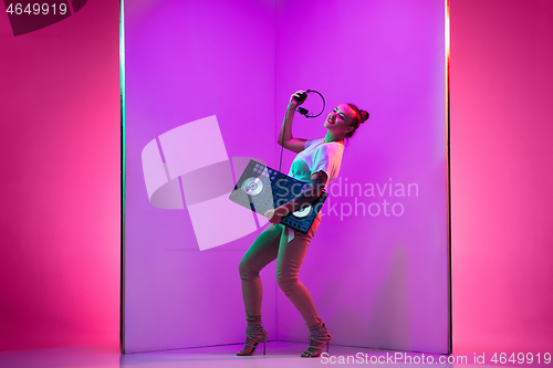 Image of Young caucasian female musician in headphones performing on purple background in neon light