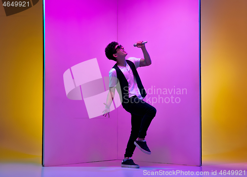 Image of Young male musician, singer performing on pink-orange background in neon light