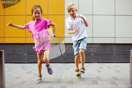 Image of Two smiling kids, boy and girl running together in town, city in summer day