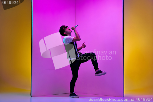 Image of Young male musician, singer performing on pink-orange background in neon light