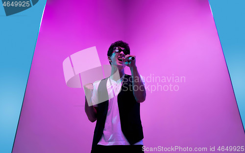 Image of Young male musician, singer performing on pink-blue background in neon light