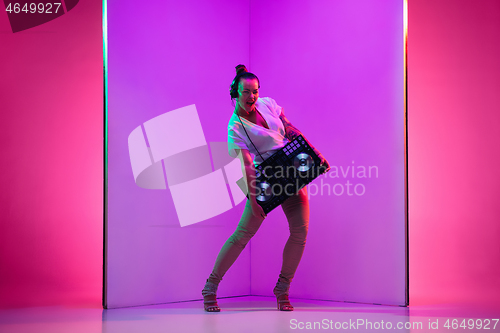 Image of Young caucasian female musician in headphones performing on purple background in neon light