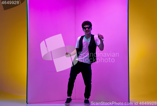 Image of Young male musician, singer performing on pink-orange background in neon light