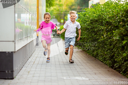 Image of Two smiling kids, boy and girl running together in town, city in summer day