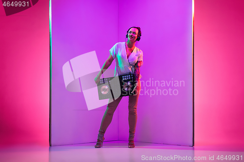 Image of Young caucasian female musician in headphones performing on purple background in neon light