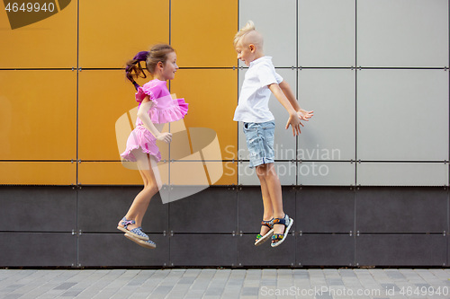 Image of Two smiling kids, boy and girl running together in town, city in summer day