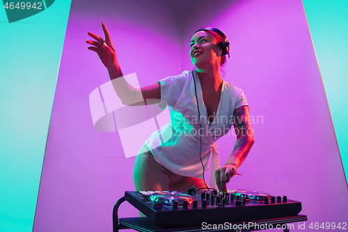 Image of Young caucasian female musician in headphones performing on purple background in neon light