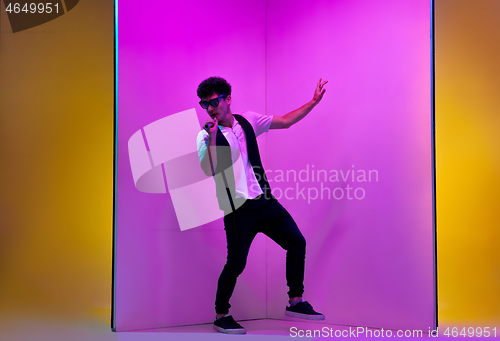 Image of Young male musician, singer performing on pink-orange background in neon light