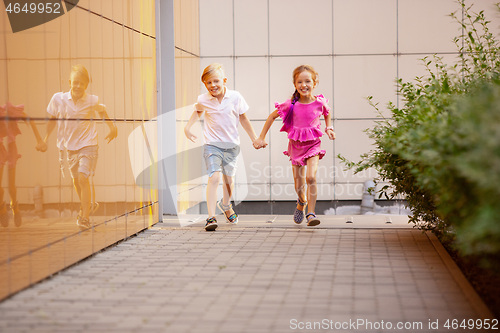 Image of Two smiling kids, boy and girl running together in town, city in summer day