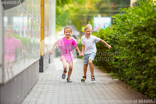 Image of Two smiling kids, boy and girl running together in town, city in summer day