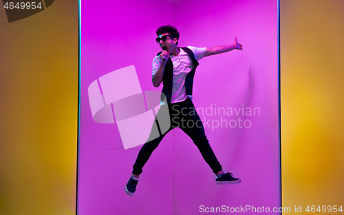 Image of Young male musician, singer performing on pink-orange background in neon light