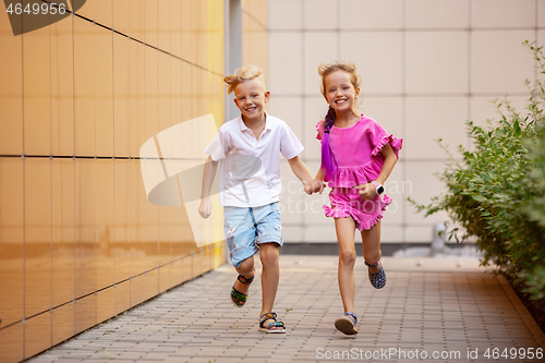 Image of Two smiling kids, boy and girl running together in town, city in summer day