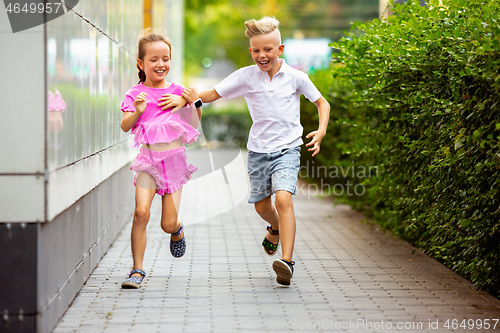 Image of Two smiling kids, boy and girl running together in town, city in summer day