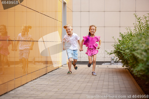 Image of Two smiling kids, boy and girl running together in town, city in summer day