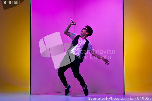 Image of Young male musician, singer performing on pink-orange background in neon light