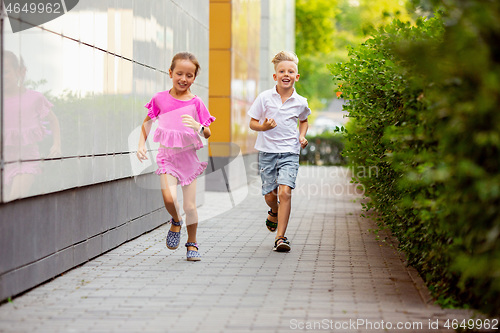 Image of Two smiling kids, boy and girl running together in town, city in summer day