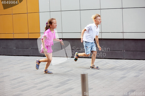 Image of Two smiling kids, boy and girl running together in town, city in summer day