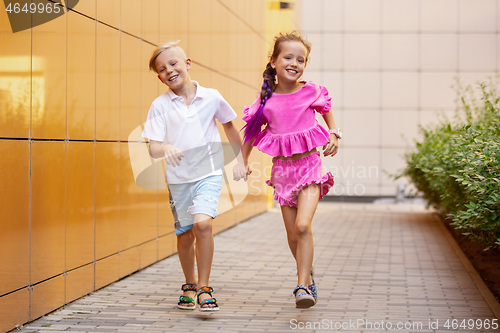 Image of Two smiling kids, boy and girl running together in town, city in summer day