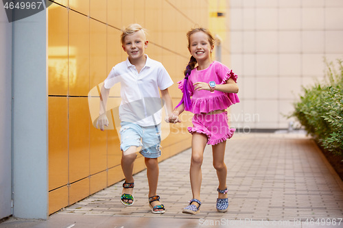 Image of Two smiling kids, boy and girl running together in town, city in summer day