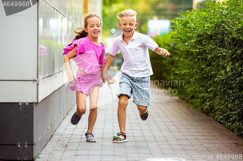 Image of Two smiling kids, boy and girl running together in town, city in summer day