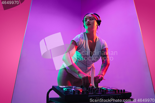 Image of Young caucasian female musician in headphones performing on purple background in neon light