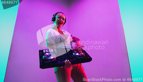 Image of Young caucasian female musician in headphones performing on purple background in neon light