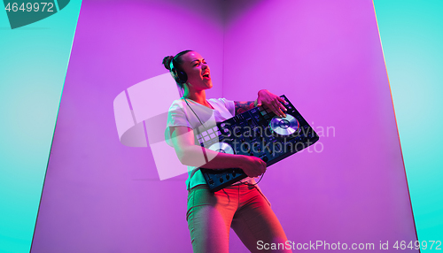 Image of Young caucasian female musician in headphones performing on purple background in neon light