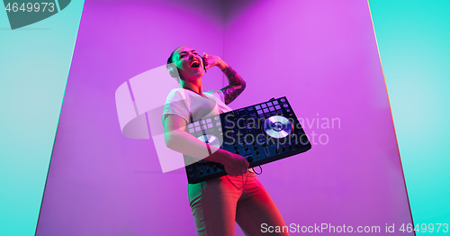 Image of Young caucasian female musician in headphones performing on purple background in neon light