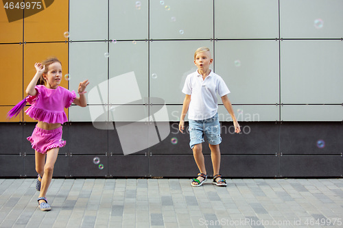 Image of Two smiling kids, boy and girl running together in town, city in summer day