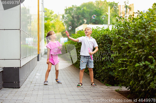 Image of Two smiling kids, boy and girl running together in town, city in summer day