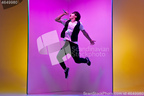 Image of Young male musician, singer performing on pink-orange background in neon light