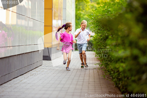 Image of Two smiling kids, boy and girl running together in town, city in summer day