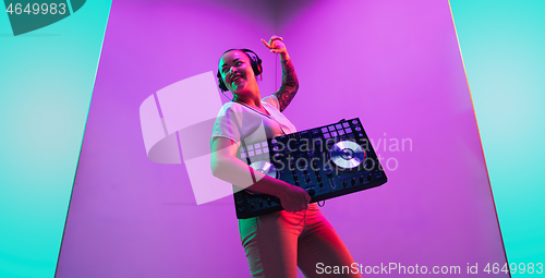 Image of Young caucasian female musician in headphones performing on purple background in neon light