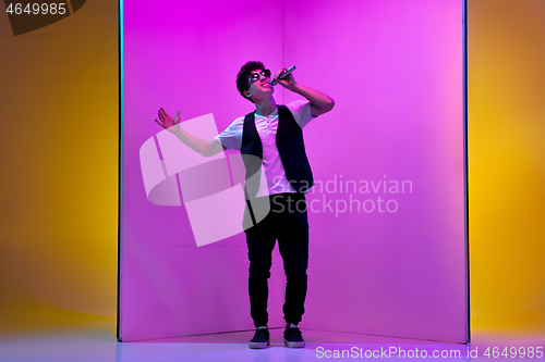 Image of Young male musician, singer performing on pink-orange background in neon light